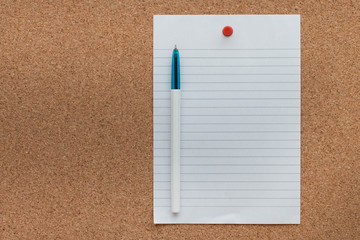 Paper pad with pen on cork board background.