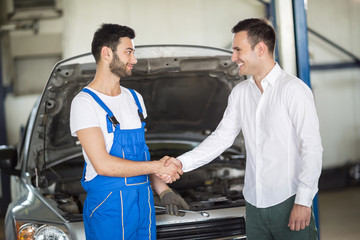 Smiling client and mechanic shaking hands - obrazy, fototapety, plakaty