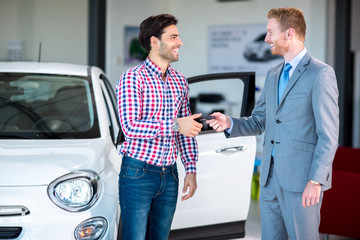 car dealer giving key of car at young male