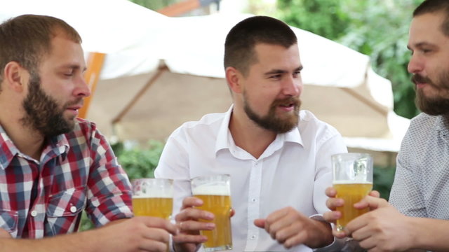 Three males outdoors in cafe talking and drinking beer