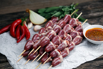 Ready to cook Duck Heart stringed on skewers BBQ with hot sauce and chili pepper. decorated with greens and vegetables. background