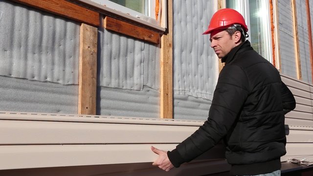 A worker installs panels beige siding on the facade of the house