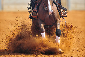 A close up view of a rider sliding the horse in the dirt