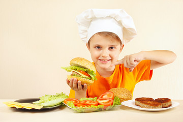 Little boy in chefs hat expressive enjoys a cooked hamburger