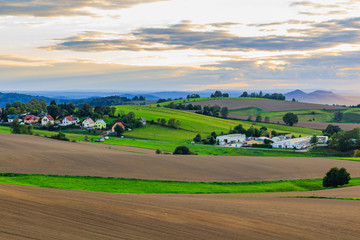 Naklejka premium Beautiful sunset over countryside landscape of rolling hills with sun beams piercing sky and lighting hillside