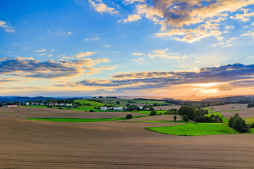 Fototapeta premium Beautiful sunset over countryside landscape of rolling hills with sun beams piercing sky and lighting hillside