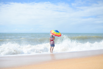 Obraz premium Beautiful young lady with rainbow umbrella walking on sunny seashore