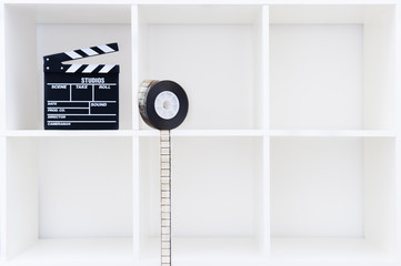 Movie clapper board and film reel on white bookshelf with cubical empty boxes