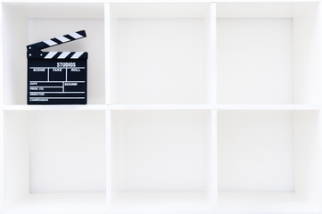 Movie clapper board on white bookshelf with cubical empty boxes