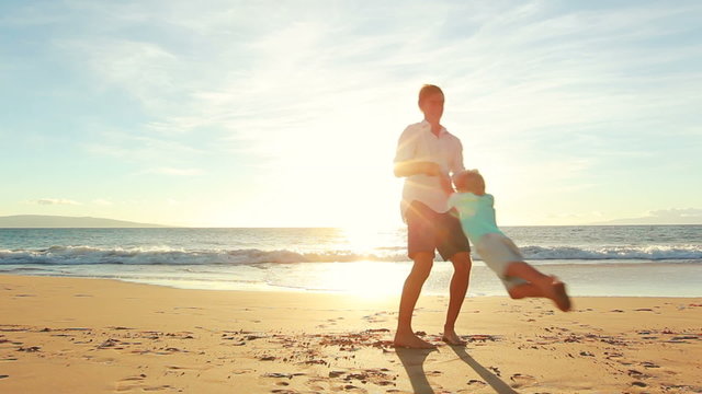 Young Father Plays With Son at the Beach at Sunset. Spinning in Circles. Summer Fun Vacation Lifestyle.