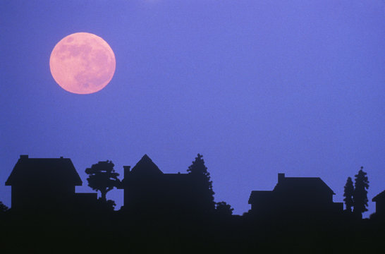 Silhouette of full moon over family homes in typical neighborhood