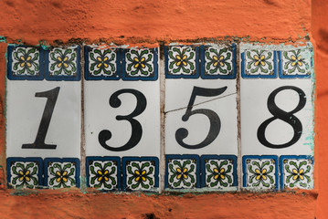 Address numbers on ornamental ceramic tiles. Decorative lettering on white background on a red wall outside