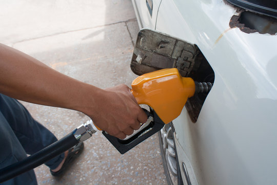 Hand hold Fuel nozzle to add fuel in car at filling station. Focus on the handle arm.