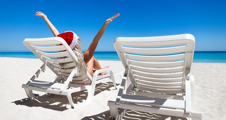 Obraz premium Happy woman in Santa Helper Hat sitting on sunbed with outstretc