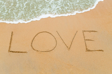 LOVE word drawn on sandy beach with wave approaching