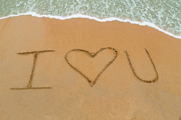 Fototapeta na wymiar I Love You drawn on sandy beach with wave approaching