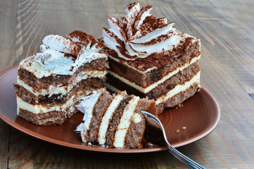 Two pieces of Tiramisu cake, one half eaten, over wooden table.