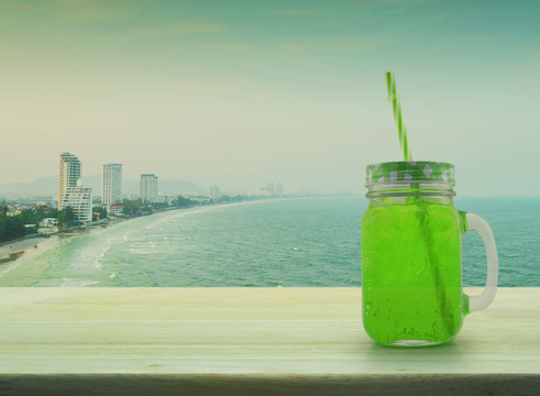 Jar with green ice drink and straw on wooden table over sea, Vin