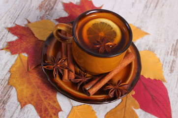 Cup of tea with lemon, spices and autumnal leaves on wooden background