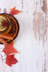 Cup of tea with lemon, spices and autumnal leaves on wooden background, copy space for text