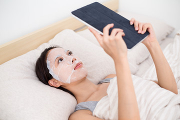 Woman using facial mask with tablet pc