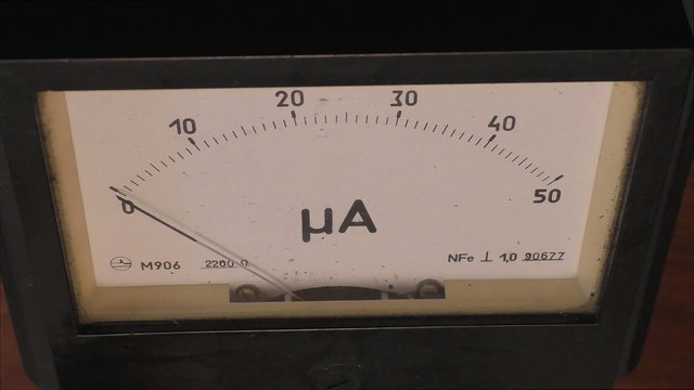 Old style micro ammeter or microamp meter close up with moving pointer showing different electric low current values while somebody is using it for measuring