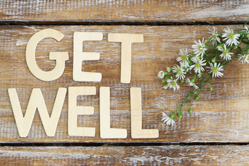 Get well written with wooden letters on rustic wooden surface and fresh chamomile flowers
