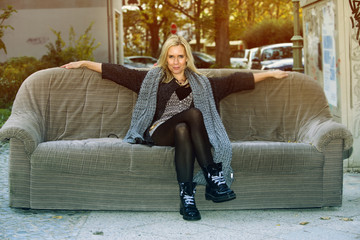 trendy woman sitting on old couch in the street