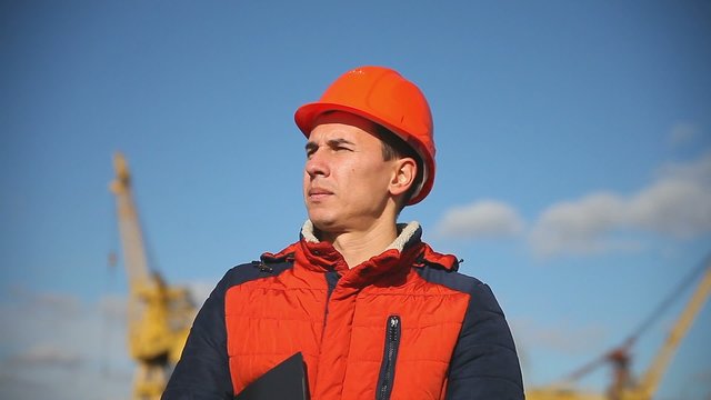 Portrait of a man construction worker in an orange helmet on a background of blue sky and construction