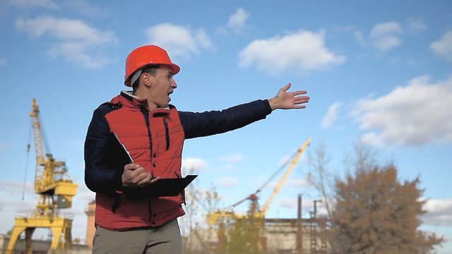 man builder construction worker in an orange helmet waving calling runs behind  crane and blue sky
