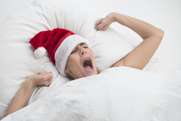 woman in bed yawning with Santa hat