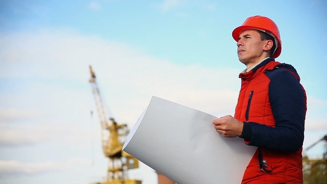man portrait builder architect in orange helmet looks instruments project against blue sky and building