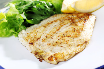 Dish of fish fillet with lettuce and lemon on table close up
