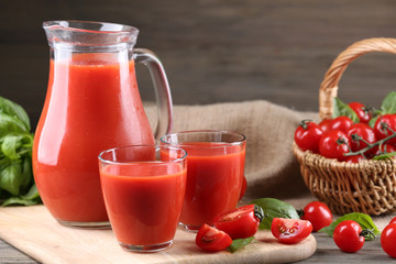 Full jug and glasses of tomato juice with vegetables on wooden table close up