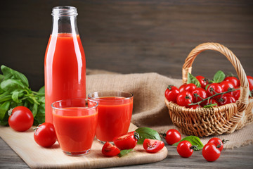 Full bottle and glasses of tomato juice with vegetables on wooden table close up