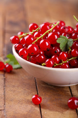 Fresh red currants in bowl on wooden table close up