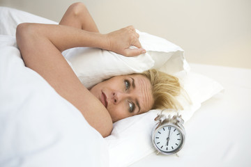 woman in bed looking at her alarm clock