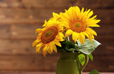 Beautiful bright sunflowers in pitcher on wooden background