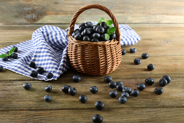 Tasty ripe blueberries with green leaves in basket on wooden table close up