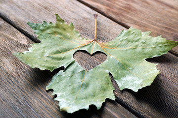 Dried autumn leaf with cutout heart on wooden background