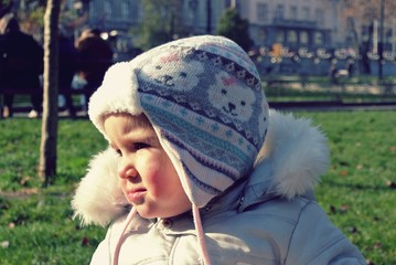 Portrait (profile) of a cute little girl in the park on a sunny day, wearing warm winter clothes and a cap. Image filtered in faded, retro, Instagram style; nostalgic, vintage childhood concept.