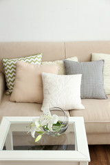 Pastel color sofa with beautiful pillows and vase with flowers on the table in front of it in the room