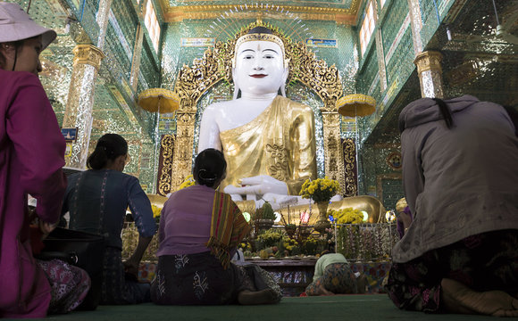Praying and bowing women in front of huge Buddha at a temple in Sagaing, Myanmar