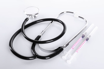 Stethoscope with syringes on white background, close up