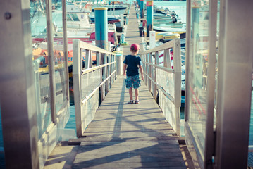 Obraz premium Backview of little boy looking at yachts from harbour gate