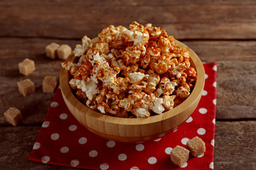 Sweet caramel popcorn in a bowl on red cotton napkin against wooden background