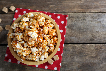 Sweet caramel popcorn in a bowl on red cotton napkin against wooden background