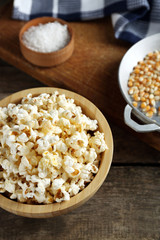Salted popcorn in a bowl decorated with kitchen equipment on wooden table