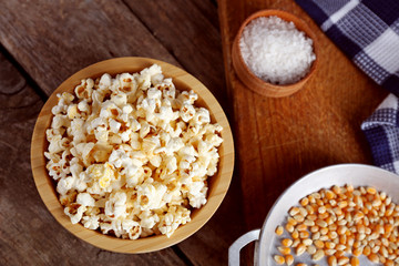 Salted popcorn in a bowl decorated with kitchen equipment on wooden table