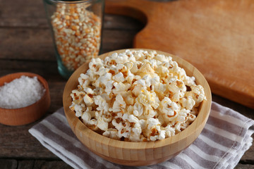 Salted popcorn in a bowl on stripped napkin with board and glass of corns on wooden table